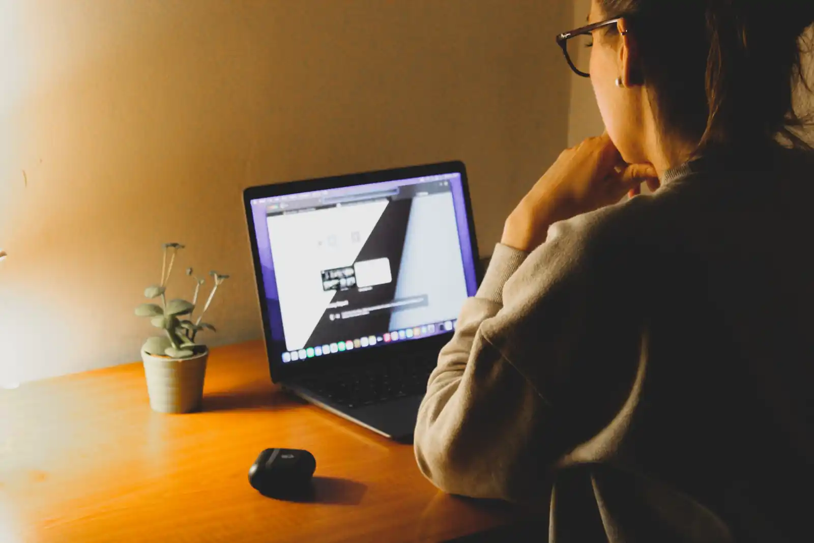 Person working on a laptop at a wooden desk in warm natural light