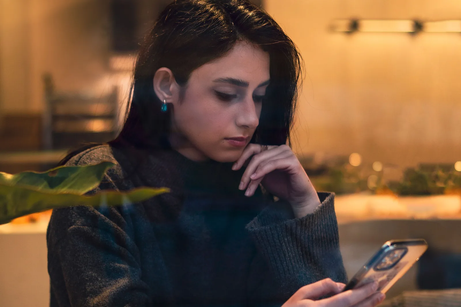 Woman reading on her phone at a table in a warmly lit cafe