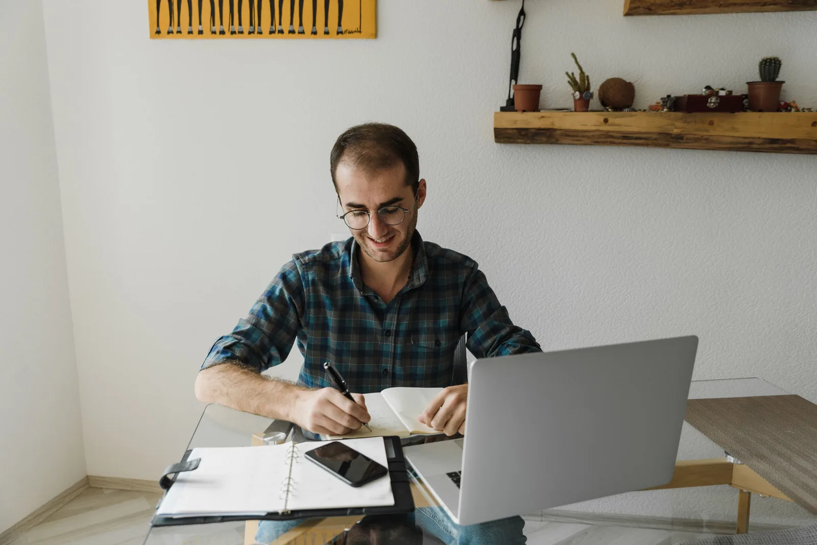 Man smiling as he writes notes next to his laptop in a home office