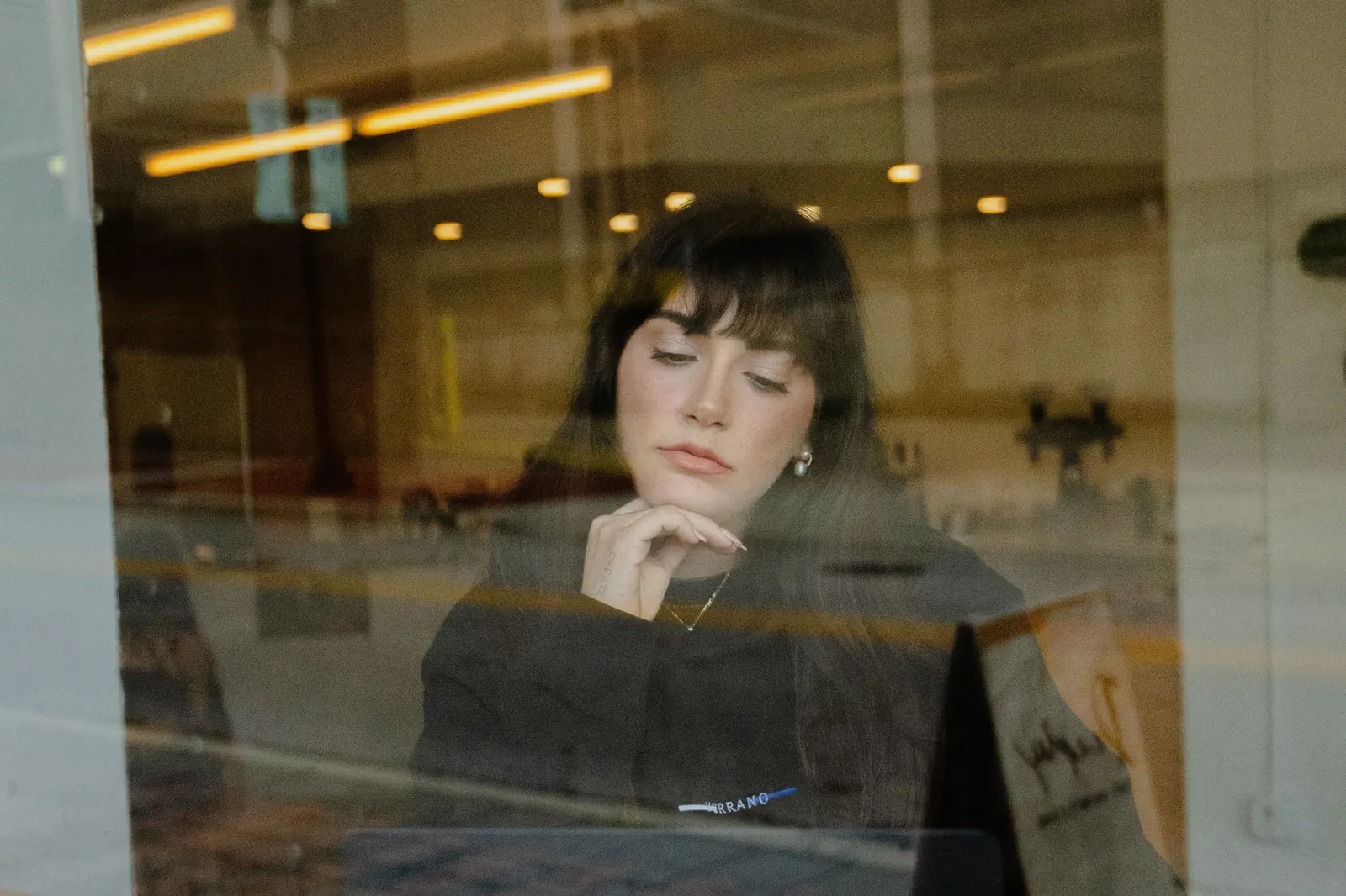 Woman working on a laptop with a coffee, seen through a cafe window