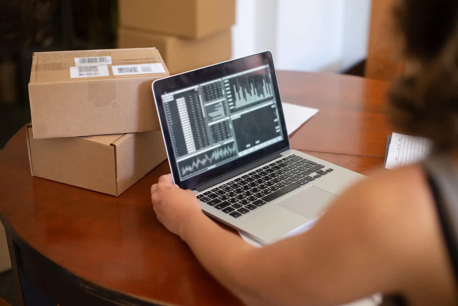 Seller reviewing orders on a laptop next to stacked shipping boxes