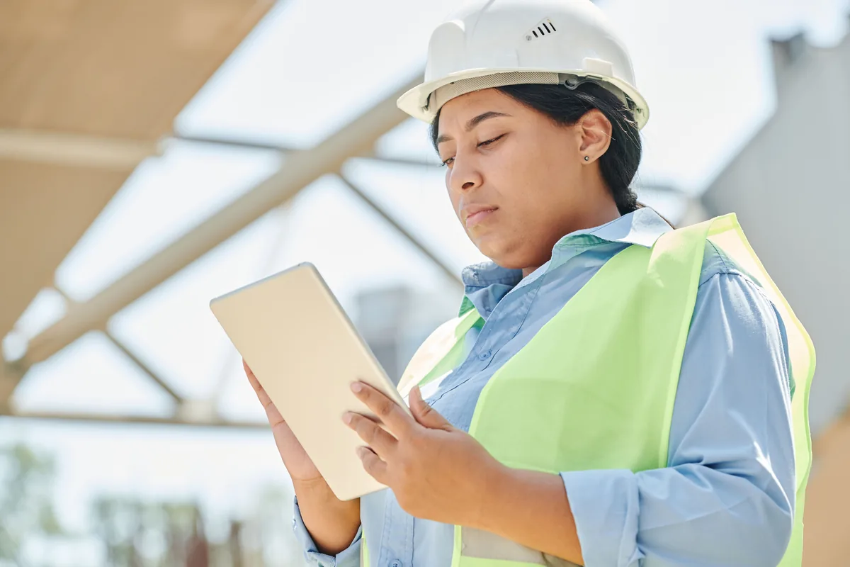 Contractor in a hard hat checking a tablet on a job site